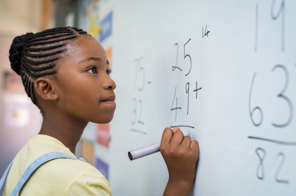 A young girl doing math on a whiteboard