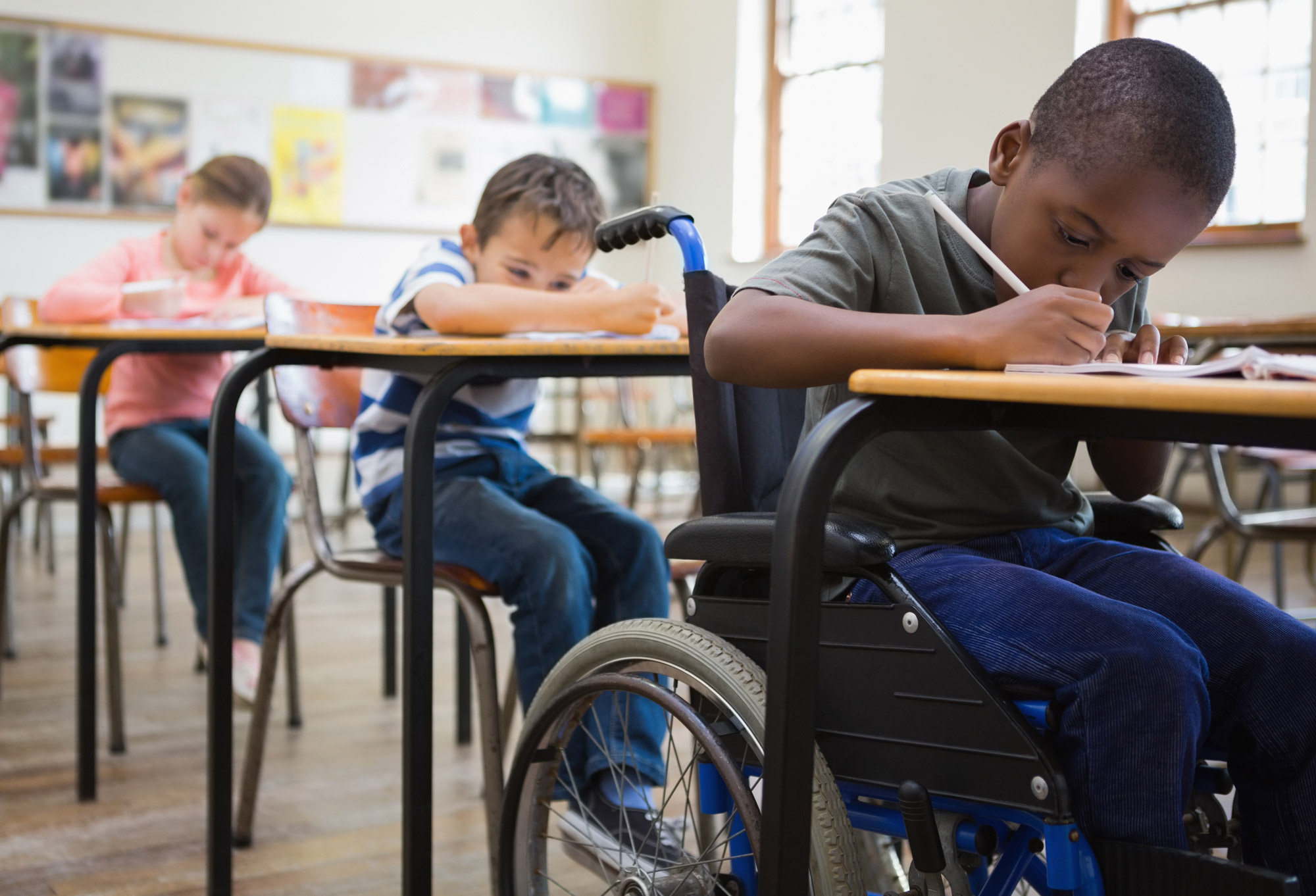 Young boy in a wheelchair writing at his desk