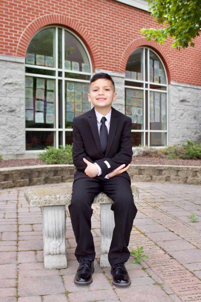 Young boy in a suit sitting on a bench and smiling